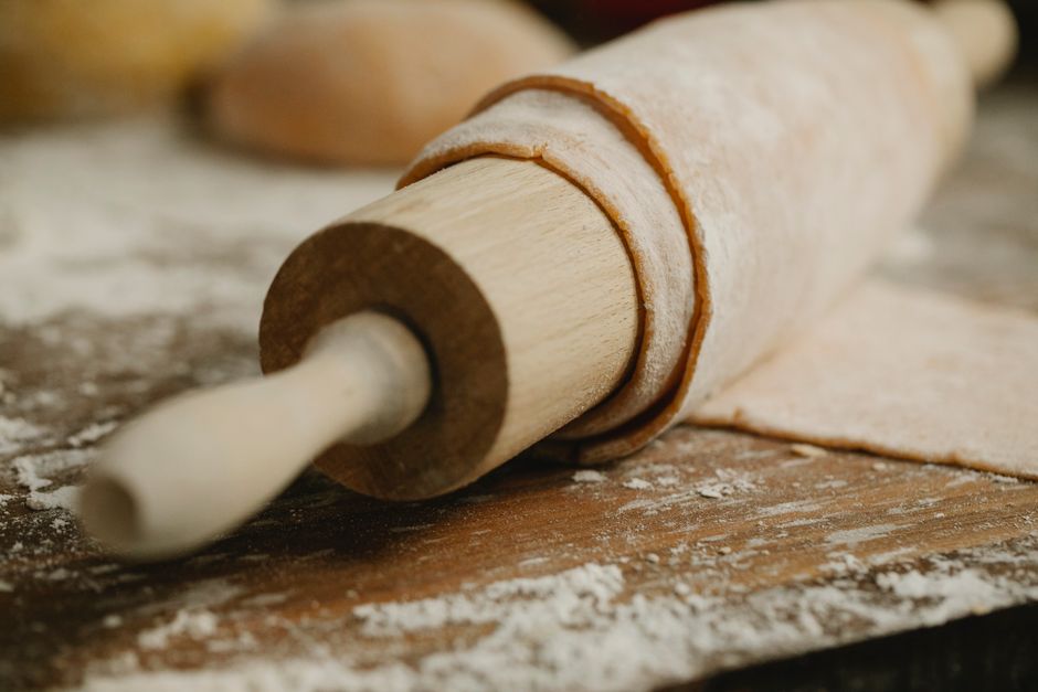 Wooden rolling pin with soft dough covered with flour on table in house kitchen